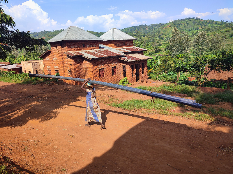 Donna in Burundi trasporta sulla testa un tubo per la costruzione del nuovo acquedotto AMU.