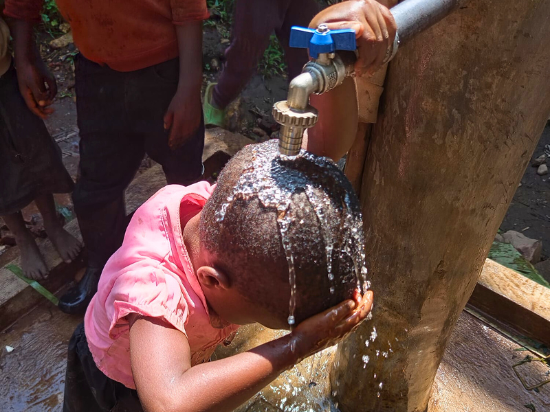 Bambina in Burundi si lava i capelli con l'acqua pulita di una fontanella riabilitata dall'AMU.