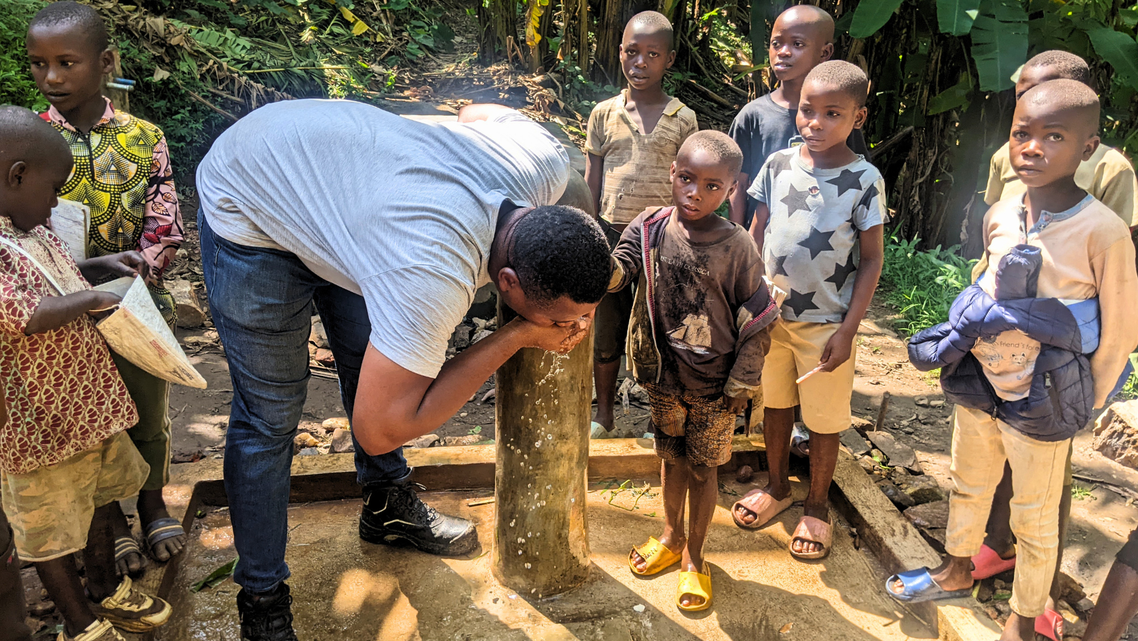 Dimitri, coordinatore del progetto, beve da una fontanella pubblica appena riabilitata a Cibitoke, circondato da un gruppo di bambini