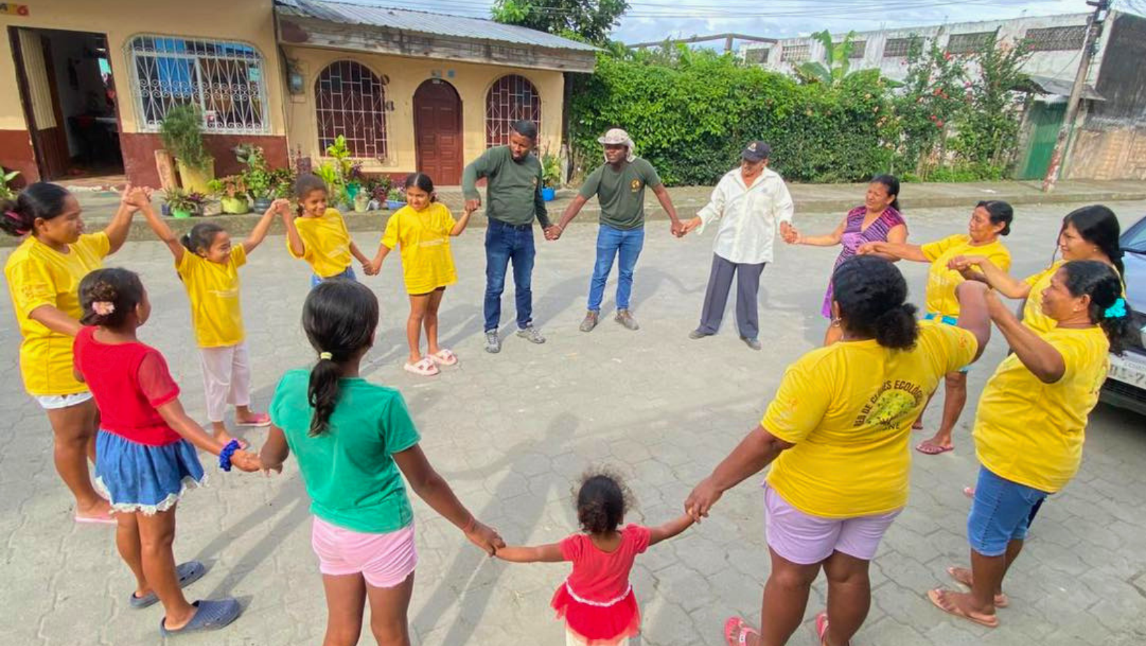 Un gruppo intergenerazionale di persone in cerchio che si tengono per mano in un giardino comunitario, con anziani, giovani e bambini che sorridono.