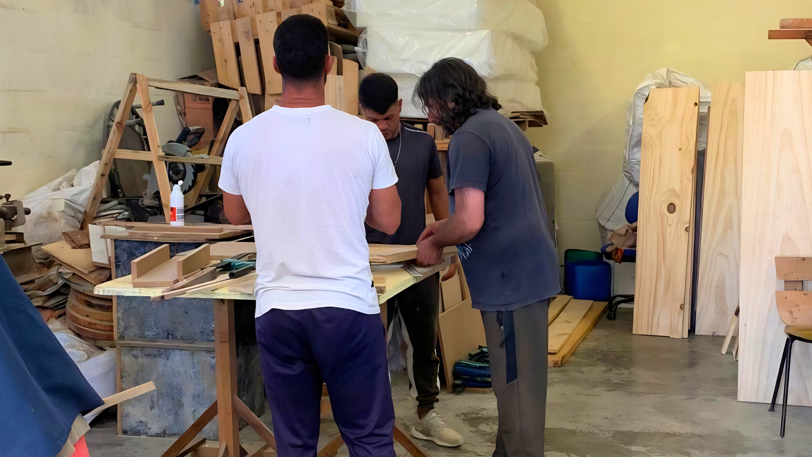 Some inmates, seen from behind, during the carpentry course of the Ripartire project in Uruguay, engaged in artisanal work for social reintegration in prisons.