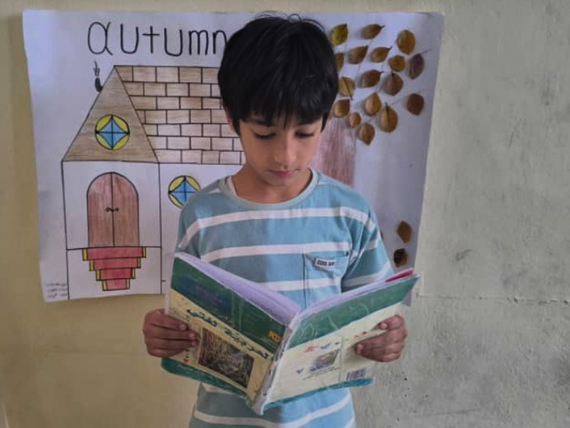Bashir, un bambino di 10 anni, tiene in mano un libro all'interno di una classe elementare in Siria.