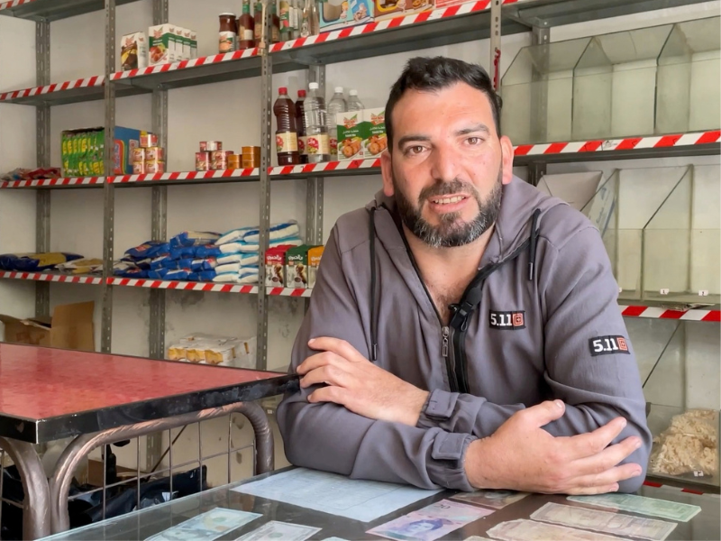 Un commerciante siriano, sostenuto dal progetto RestarT, posa dietro il bancone del suo negozio di alimentari.