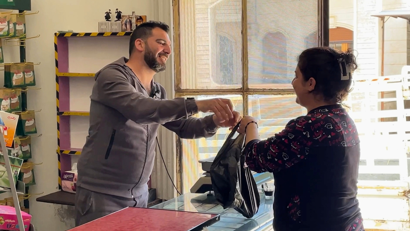 Tony Jarouj, proprietario del negozio sostenuto da RestarT in Siria, sorride mentre consegna una borsa nera a una cliente.